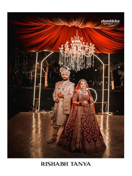 A formal, album-cover style portrait of the couple on their wedding stage, set against a backdrop of red drapes and a crystal chandelier.