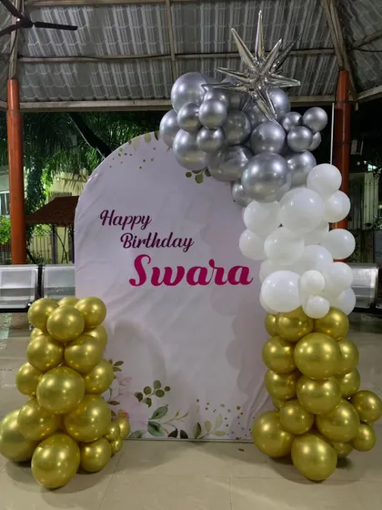 A modern setup with a custom-printed arch backdrop and an asymmetric balloon arrangement in gold, white, and silver.