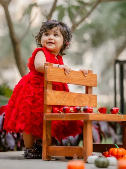 A duplicate of image 12, capturing a baby girl in a beautiful red dress during her outdoor first birthday celebration.