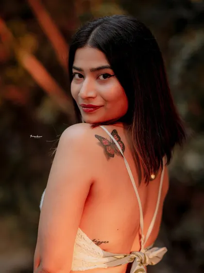 A candid-style portrait with a warm, golden hour glow. The focus on the butterfly tattoo adds a personal and interesting detail to this back profile shot.