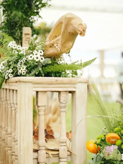 A detail shot from the brunch, showing a rustic wooden balustrade decorated with dried palm leaves and fresh greenery. The design focuses on texture and natural elements to create a simple yet elegant look.