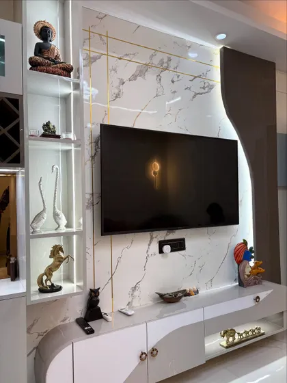 This TV unit features a white marble-finish back panel with elegant gold inlay work. The design includes open shelves for displaying decor, like the Buddha statue, and closed cabinets for clutter-free storage.