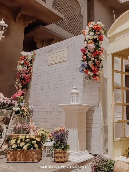 An elaborate floral decor setup with a vintage bicycle and a classic telephone booth creates a whimsical photo corner at a Jaipur wedding.