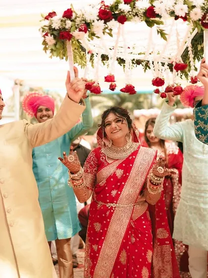The bride dances with joy under the phoolon ki chadar, surrounded by her enthusiastic brothers.
