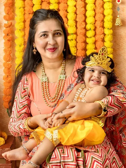 A heartwarming photo of a mother and her smiling baby dressed as Krishna, both radiating joy.