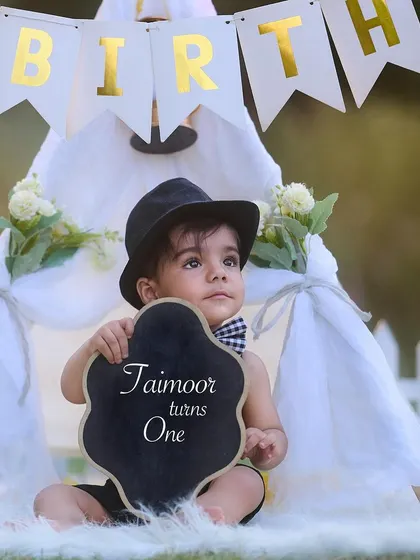 Dressed up and ready to celebrate turning one. This little gentleman is holding a sign to announce his big day in front of a classic white picket fence and teepee setup.
