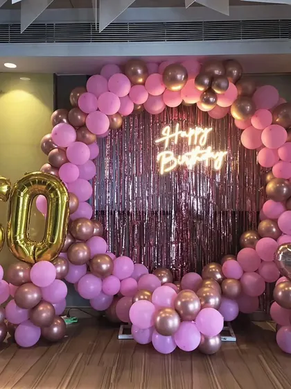 A vibrant 60th birthday decoration with a pink and rose gold balloon ring, a shimmer backdrop, and large gold foil '60' balloons.