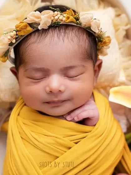 A close-up shot of a newborn's sweet smiling face. I focus on capturing these fleeting expressions that you'll want to remember forever. The floral headband adds a perfect touch.