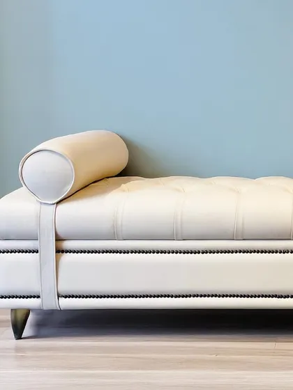 An elegant off-white upholstered bench with clean lines and classic details. The tufted seat, bolster pillows, and nailhead trim make it a sophisticated and timeless piece for an entryway or bedroom.