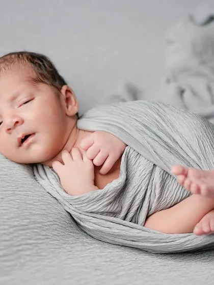 Drifting off to sleep. This image captures that in-between moment of a newborn settling, with his tiny hands held close, wrapped in a soft grey swaddle.
