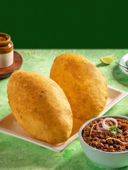 A classic Punjabi dish of Chole Bhature, with fluffy bhaturas and spicy chickpea curry, styled against a vibrant green background.