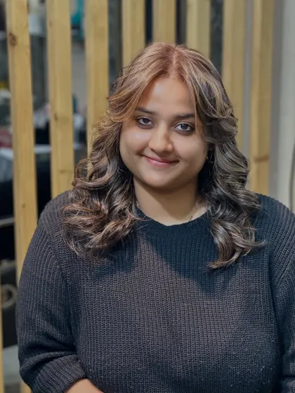 The client is all smiles after her hair color transformation. This photo captures the final look, featuring soft curls that enhance the new highlights.