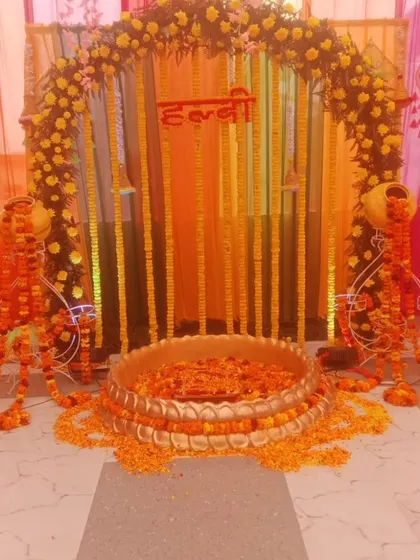 A traditional Haldi ceremony setup inside a home. The decor features a marigold arch, hanging flower strings, and a large brass urli placed on a marble floor, showing how I can adapt to any space.