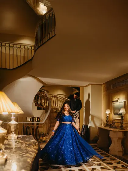 A grand, sweeping shot of Raakhee on the staircase in her dazzling blue lehenga, with Akshay in the background. A true fairytale moment.