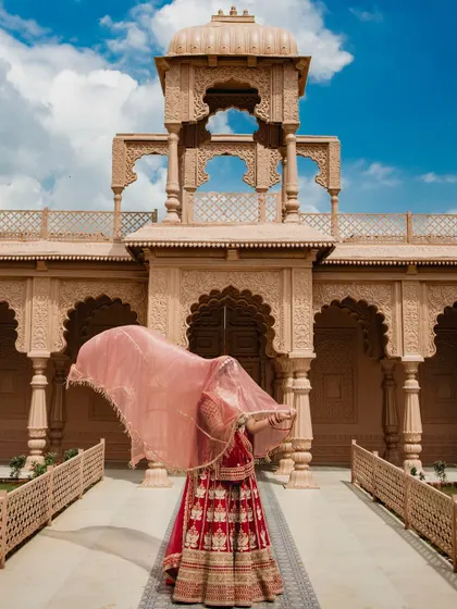 A creative bridal portrait where the bride's face is hidden by her flowing veil. This artistic shot against the grand building creates a sense of mystery and elegance.