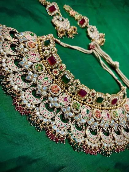 Red for love, green for new beginnings. This complete bridal set tells a story with its colorful Meenakari work, featuring a statement necklace and matching maang tikka.