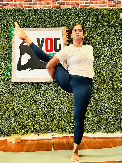 A student practices a standing balancing pose, demonstrating focus and stability while binding her arm behind her back.