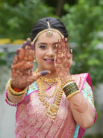 A playful and happy bride showing off her intricate henna. Her hair is styled in a traditional updo, a classic choice that keeps the focus on her radiant face.