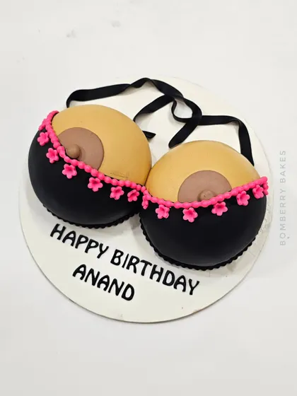 A "Happy Birthday Anand" cake with a playful, adult theme, featuring a sculpted bra.