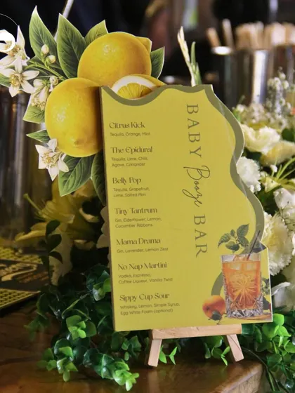 The 'Baby Booze Bar' menu nestled amongst fresh flowers and greenery, showcasing a cohesive and beautifully styled beverage station.