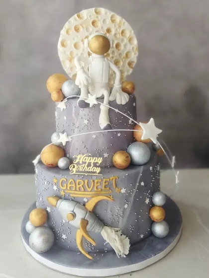 An out-of-this-world cake for a space-themed birthday! This two-tier creation features an astronaut chilling on the moon, surrounded by planets and stars, perfect for a little explorer's big day.