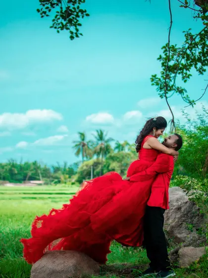 A vibrant and romantic pre-wedding photo with the groom lifting the bride, her red dress standing out against the green landscape.