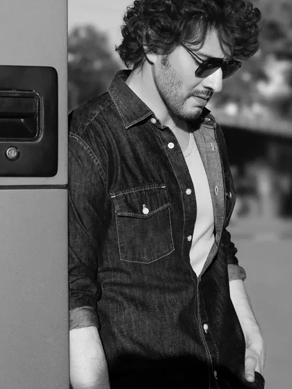 A black and white version of a behind the scenes shot with Mahesh Babu. Stripping away the color brings a different mood to the image, highlighting the texture of his denim shirt and his contemplative pose.
