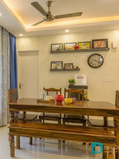 The dining area is simple and functional, with a six-seater wooden table and a gallery wall for family photos.