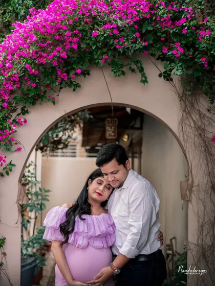 A portrait of comfort and love. The mother-to-be rests her head on her partner's shoulder, framed by a beautiful arch of pink flowers.