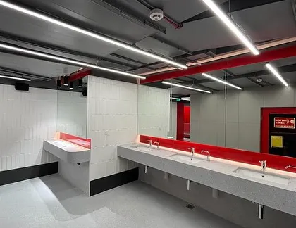 The wet area washroom is designed with a clean, industrial look. A long concrete-finish vanity, minimalist fixtures, and linear lighting are accented with a bold red mirror frame, tying it to the gym's overall color scheme.
