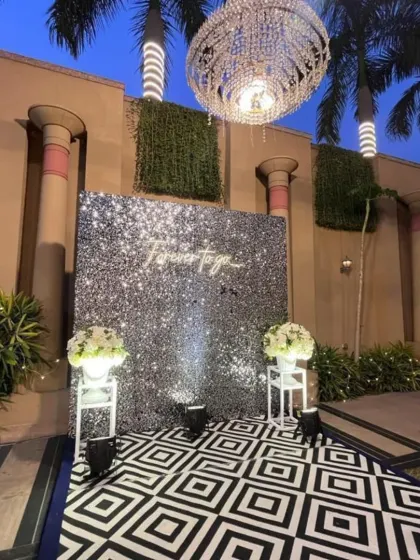 A modern and chic photo wall with a "Forever to go" neon sign against a silver sequin backdrop. The geometric floor adds a trendy touch to this reception setup.