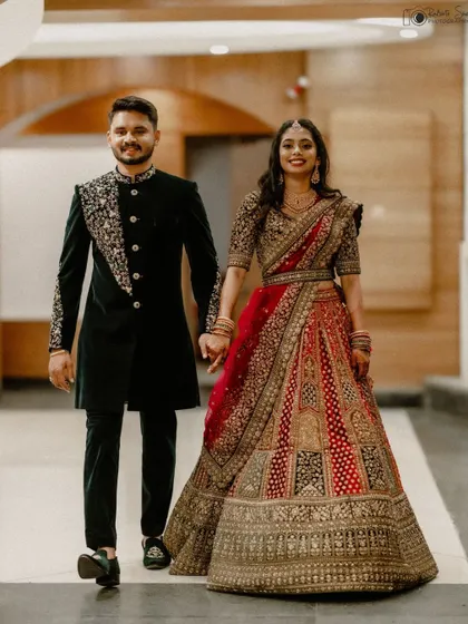 A full-length shot of the couple walking hand in hand, showcasing their stunning reception outfits. The bride's intricate lehenga and the groom's coordinated sherwani make for a grand and stylish wedding portrait.