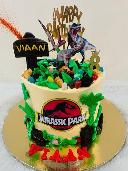 A prehistoric adventure with this Jurassic Park themed cake. It's perfect for a dinosaur lover, complete with a T-Rex, lush green foliage, and the iconic park logo.