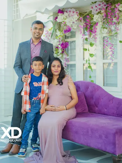 A formal family portrait with their son, taken in an elegant indoor studio with a purple chaise lounge.