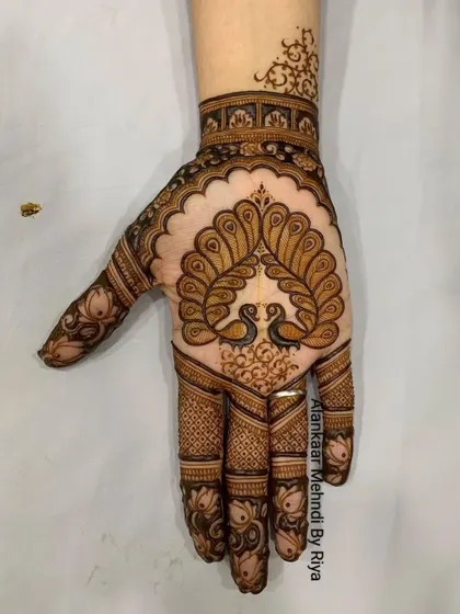 A beautiful design for the back of the hand, with two peacocks forming a heart shape with their necks, perfect for an engagement or sangeet.