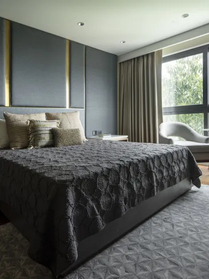 This bedroom at the Jor Bagh Residence features a dramatic headboard with dark fabric panels and brass accents. The design is a study in sophisticated comfort, with a rich, layered color scheme and luxurious textiles.