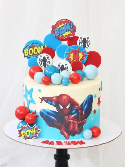 An action-packed Spider-Man cake bursting with color. This design features a large Spidey graphic, comic book action words, and a cascade of red and blue spheres.