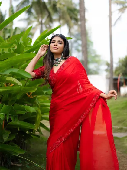 A full-length portrait that shows the graceful flow of the red saree. The natural garden setting provides a perfect, serene backdrop.