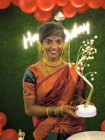 A happy customer dressed in traditional attire for her birthday celebration, posing with our 'Green Dream' decor and a 'Happy Birthday' neon sign.