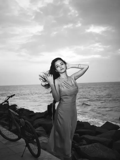 A black and white beach portrait of a woman in a silk dress, with the wind blowing through her hair. The ocean and a bicycle in the background add to the relaxed, breezy atmosphere of this fashion shot.