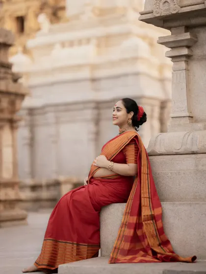 Seated on the temple steps, this mother-to-be looks radiant in her red saree, capturing a moment of quiet joy and anticipation.
