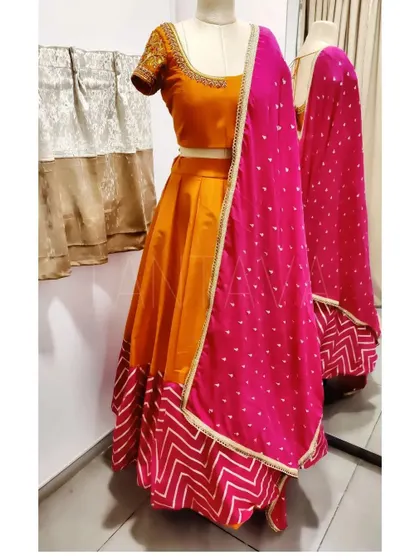 A vibrant and festive lehenga set on a mannequin. This piece was custom-made with a chevron-print border, a solid orange skirt, and a contrasting pink dupatta with delicate embroidery.