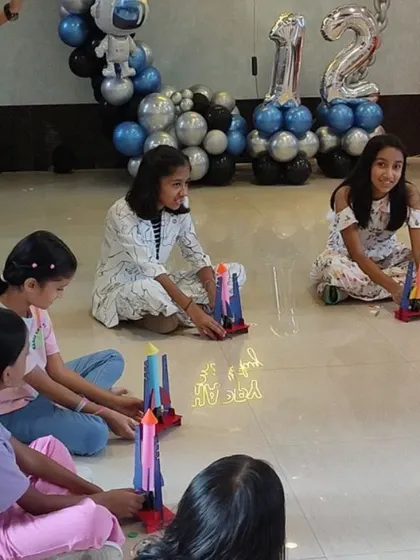 A space-themed birthday party in full swing, with astronaut balloon decor and a row of girls ready to test their newly built rockets.