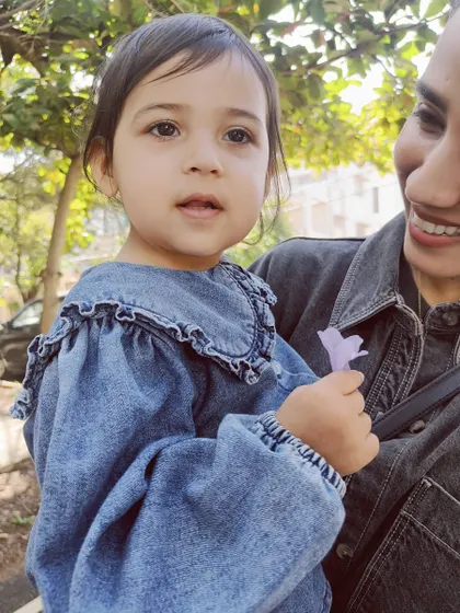 A toddler holds a flower she found on her walk, a small treasure from her exploration of nature.