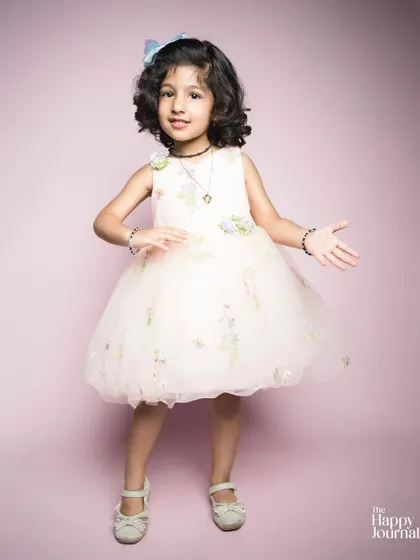 A little girl in a beautiful embroidered dress, posing with her hands on her hips. A portrait full of charm and personality.