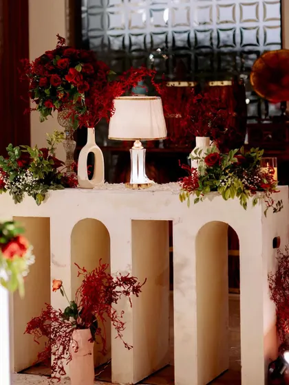A close-up of the decor details, including the modern console table, minimalist vases, and a classic table lamp, all surrounded by rich red florals.
