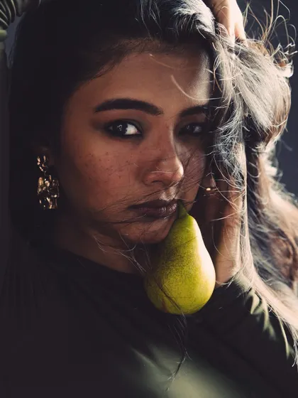 An unconventional beauty shot using a pear as a prop. This kind of creative portrait is designed to be memorable and artistic for editorial use.