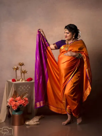 The way she holds the pallu of her saree shows its beautiful color and texture, adding a dynamic element to the portrait.