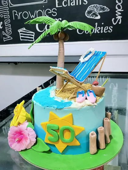 Another angle of the 50th birthday beach cake, showing the "50" sign and the handcrafted details like the tiny slippers and coconut drink.