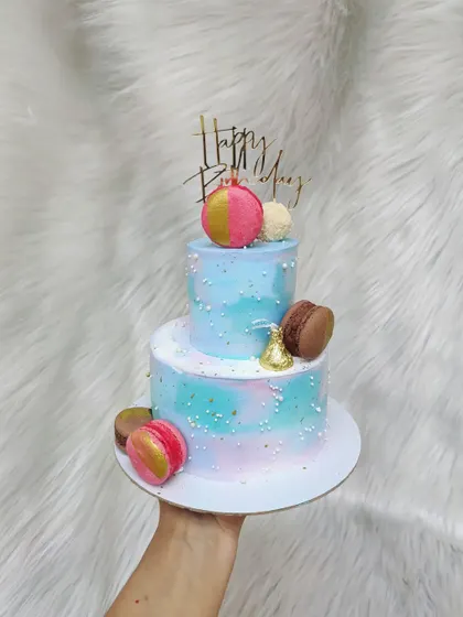 Another mini two-tier cake, this one with a blue and pink watercolor effect. It's decorated with macarons and Hershey's Kisses for a sweet touch.
